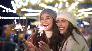 Two women holding sparklers, smiling, night fair.