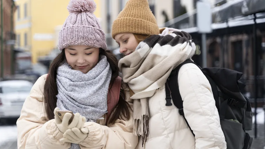 Zwei Personen schauen auf Handy, Winterkleidung.