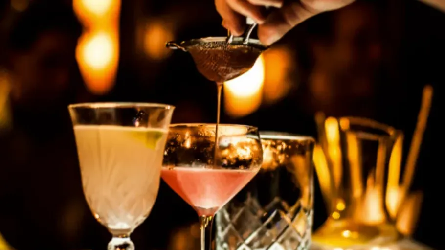 Cocktails being poured with strainer at bar.