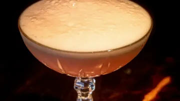 Champagner-Cocktail mit Schaumkrone, dunkler Hintergrund.