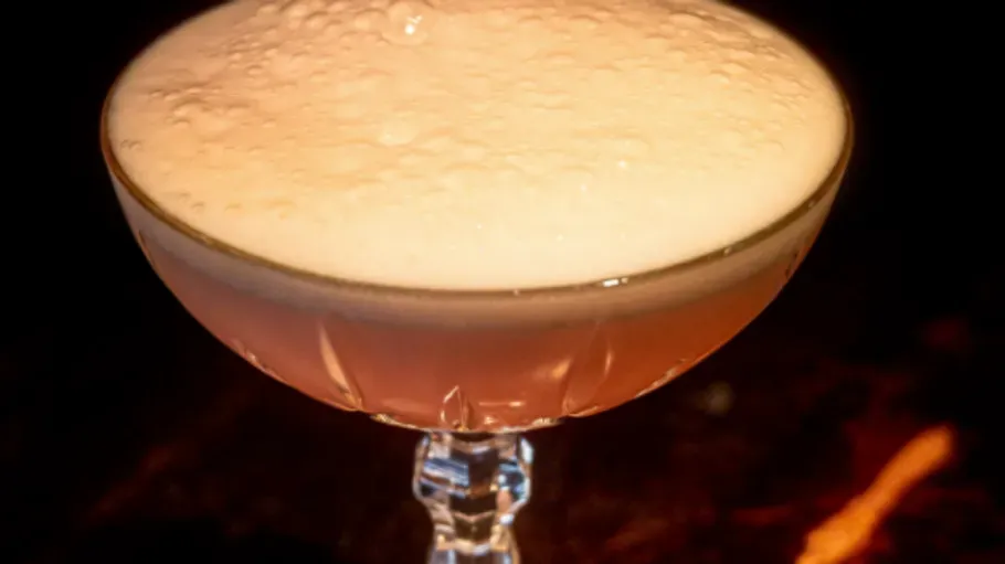 Champagner-Cocktail mit Schaumkrone, dunkler Hintergrund.