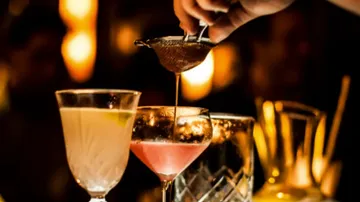 Cocktails being strained at a dimly lit bar.