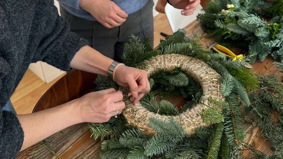 Person crafting a wreath on wooden table.