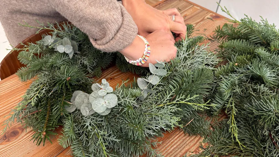 Hände arrangieren einen Kranz auf Holztisch.
