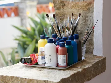 Paints and brushes stand on a stone slab outside.