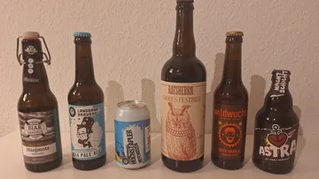 Six beer bottles and cans on a table.