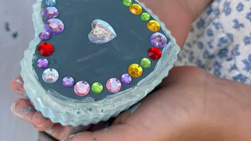 Heart-shaped craft with colorful gems held by hands.