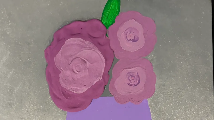 Purple clay flowers with green leaves on gray background.