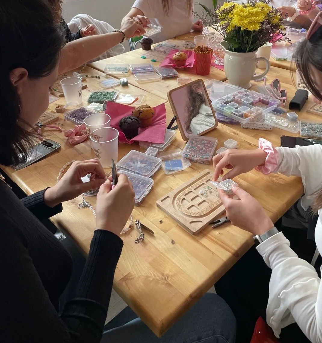 Leute basteln Schmuck an einem Holztisch.