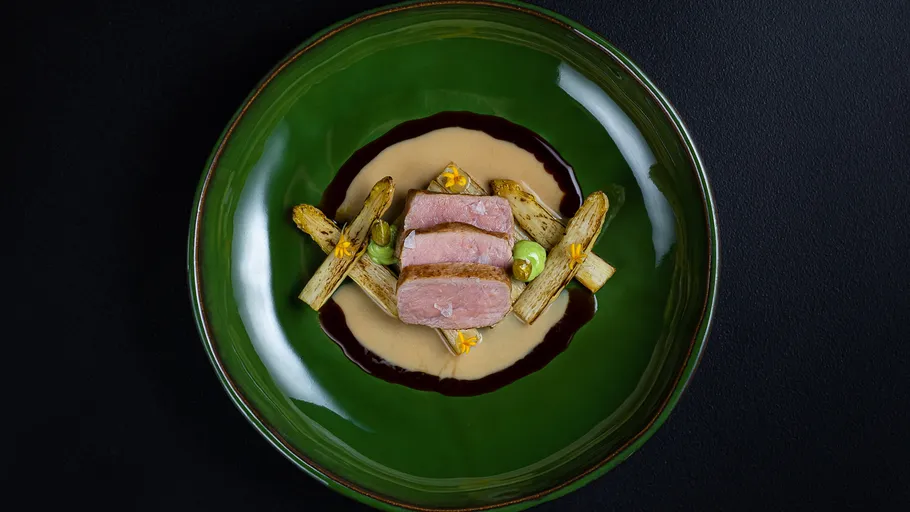 Elegantes Gericht mit Fleisch und Gemüse auf grünem Teller.