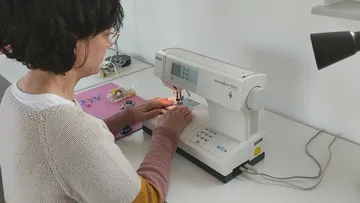 Frau näht an einer weißen Nähmaschine.