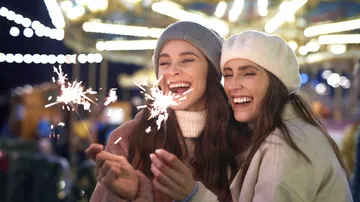 Two women smiling, holding sparklers at night.