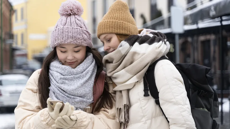 Zwei Frauen in Winterkleidung schauen auf Handy.