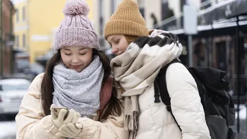 Zwei Frauen in Winterkleidung schauen auf Handy.