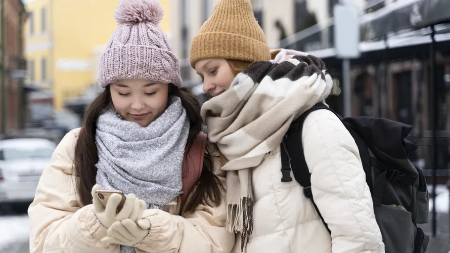 Two women in winter clothes look at phone.