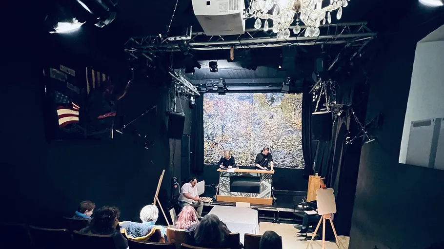 Kleines Theater mit Publikum und zwei Darstellern auf Bühne.