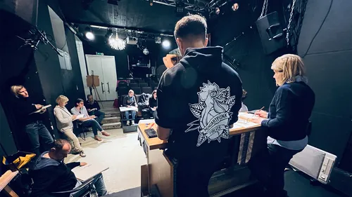 Menschen proben auf Bühne in dunklem Theater.