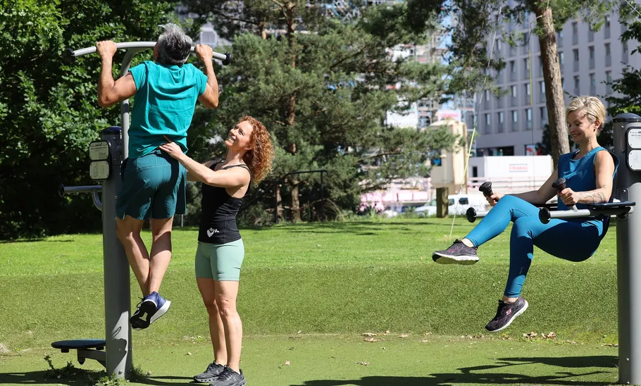 Drei Personen trainieren in einem Freiluft-Fitnessstudio.