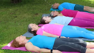 Menschen liegen auf Yogamatten im Freien.