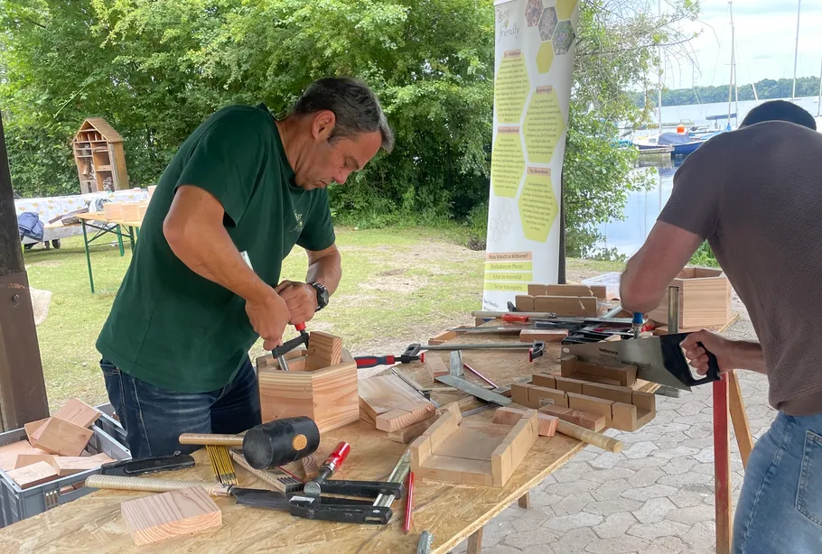 Männer arbeiten mit Holz an einem Außentisch.