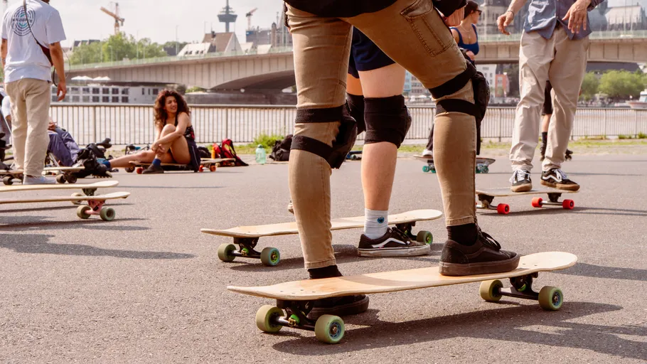 Skateboarders practicing by a riverside bridge.