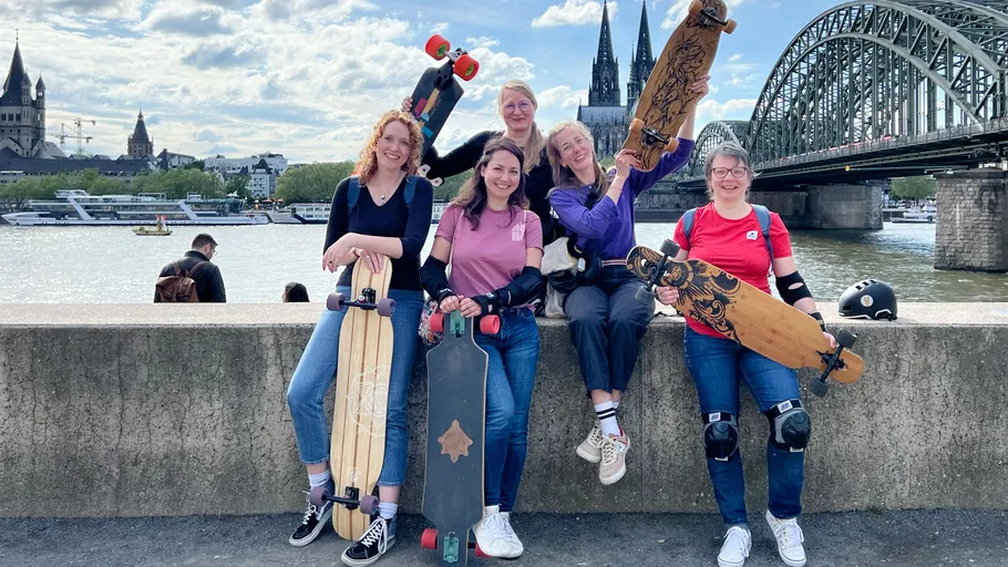 Five people with longboards by a bridge.