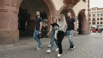 Four people walking near historic arches.