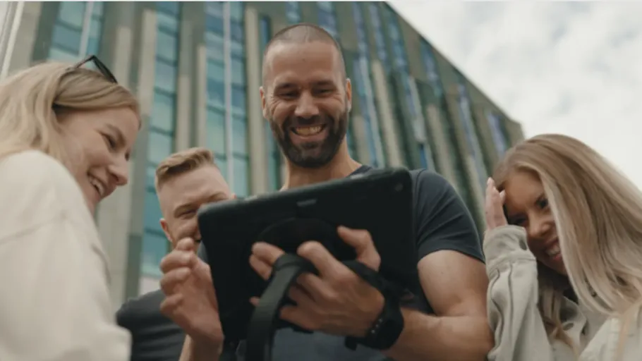 Gruppe von Menschen lächelt um ein Tablet draußen.