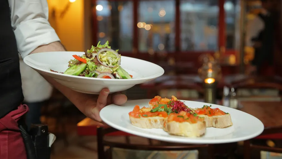 Waiter serves salad and bruschetta in restaurant.