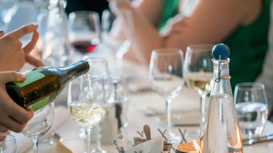 Person pouring wine at a dinner table.