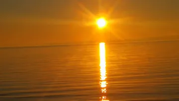 Sonne untergeht über ruhigem Ozean.