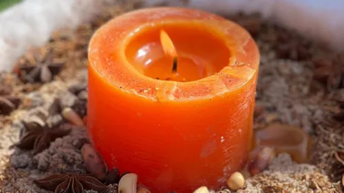 Orange Kerze umgeben von Gewürzen und Nüssen.
