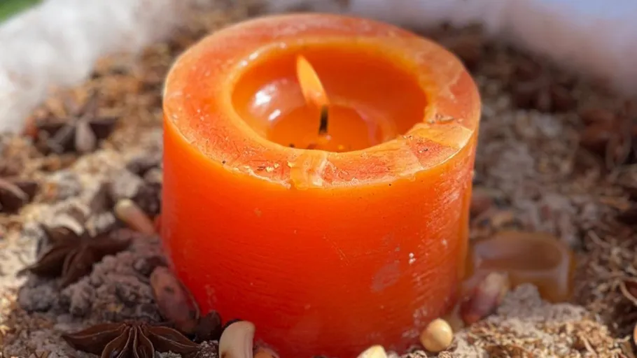 Orange Kerze umgeben von Gewürzen und Nüssen.