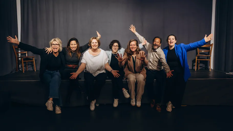 Sieben Personen sitzen, lächelnd, freudige Ausdrücke.