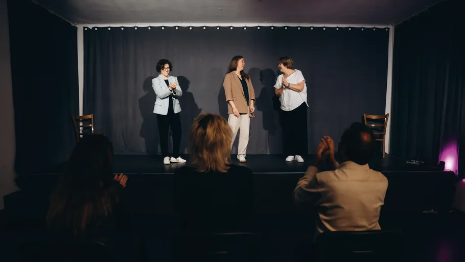Three people on stage, audience clapping.