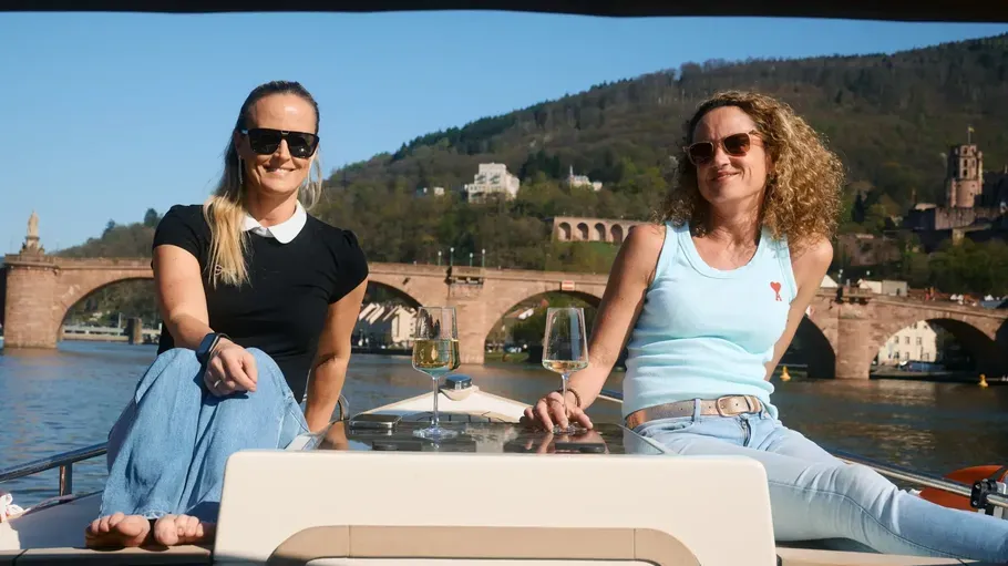 Zwei Personen sitzen auf einem Boot, Brücke dahinter.