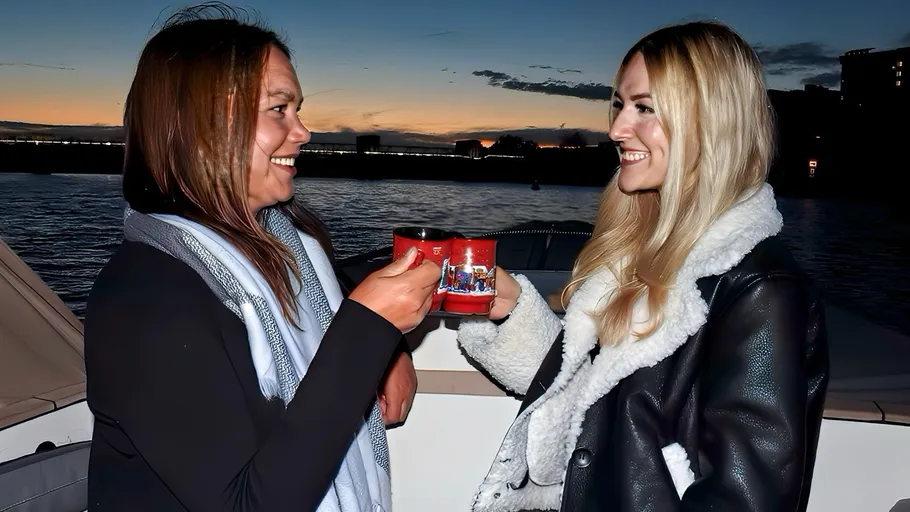 Two people clinking mugs on a boat at sunset.