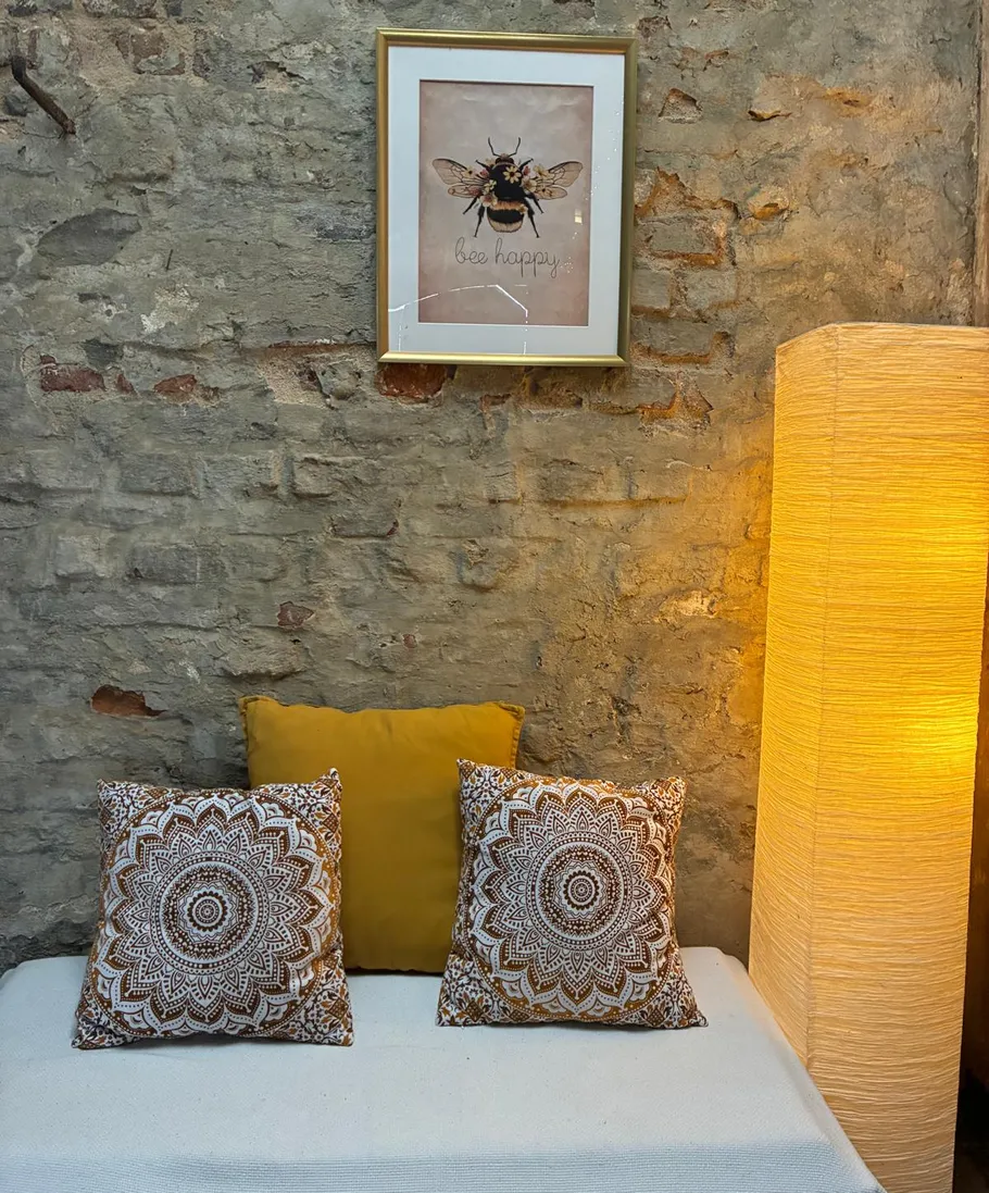 Couch with pillows, poster, and lamp in room.