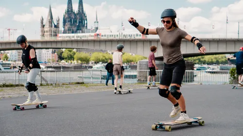 People skateboarding near a river with a bridge.