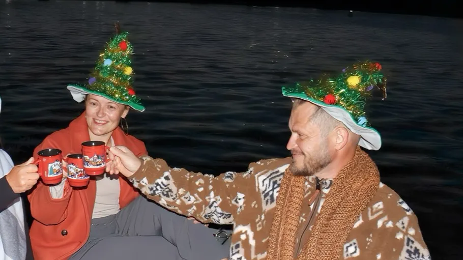 Two people wearing festive hats clinking cups, outdoors.