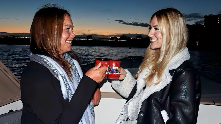 Two women toasting mugs on a boat.