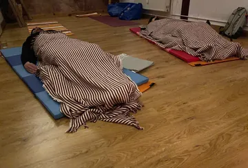 Personen schlafen auf Matten, Holzfußboden.