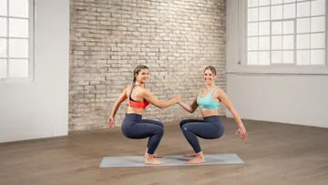 Two women squatting, holding hands in studio.