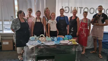 Group smiling in pottery studio with creations.