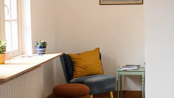 Gemütlicher Stuhl mit Kissen in hellem Raum.
