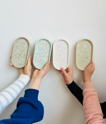 Hands holding colorful terrazzo trays against wall.