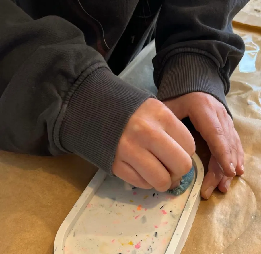 Person sanding a colorful tray on table.