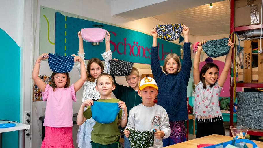Children holding handmade pouches in a craft room.