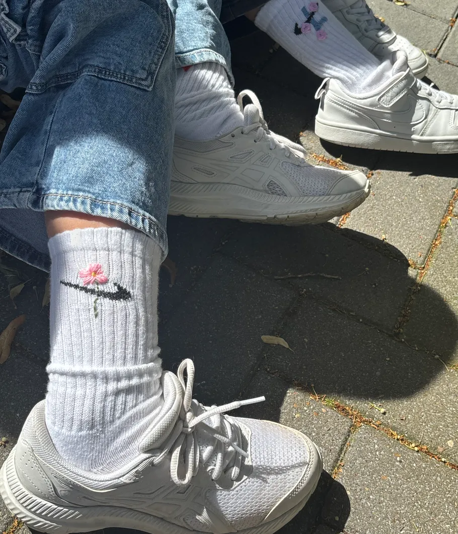 Weiße Turnschuhe und Socken mit Blumenmuster auf Pflaster.