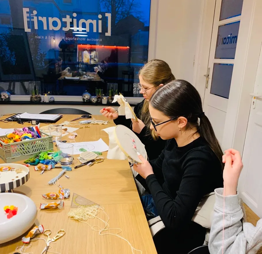 People embroidering at a wooden table indoors.